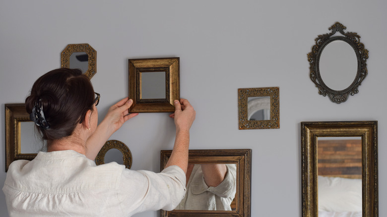 a woman hanging a small square mirror on the wall