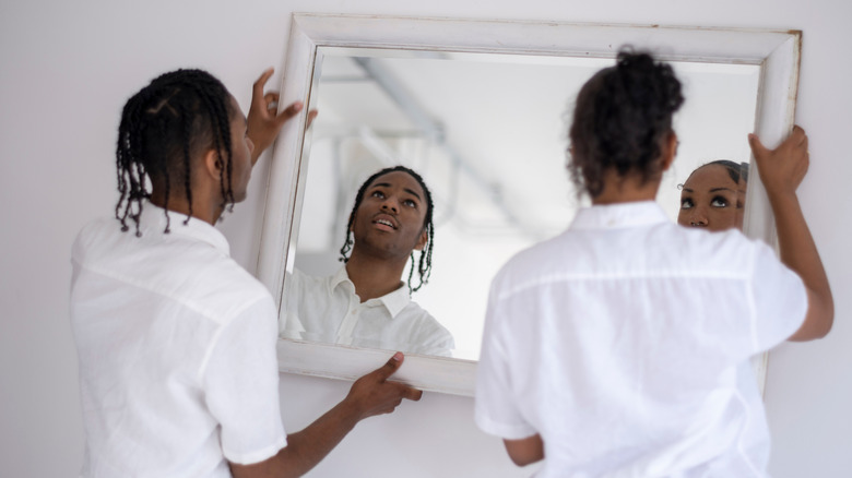 Girl and boy hanging a white rectangular mirror up on the wall