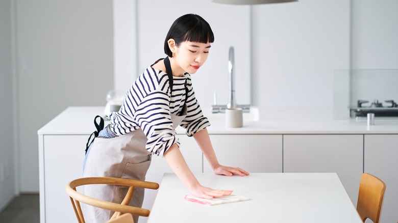 Woman wiping down kitchen table with a dishcloth