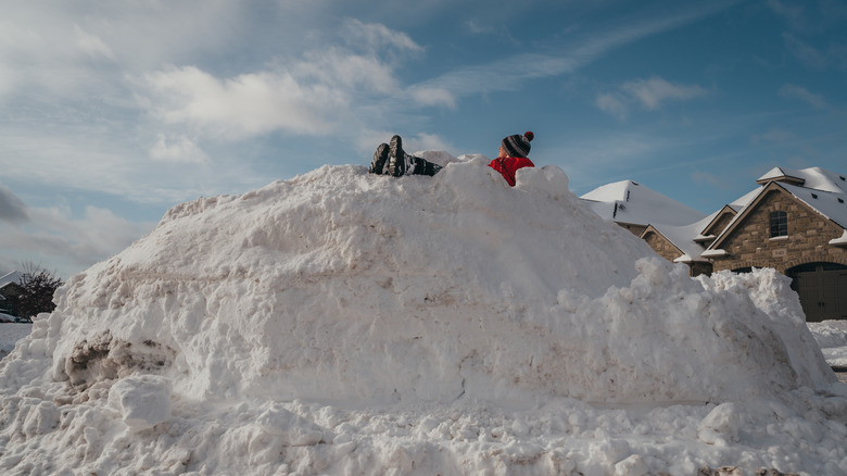 A person sits on top of a large pile of snow.