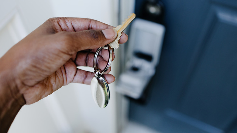 A person holding a set of keys with an open, door-mounted lock box in the background