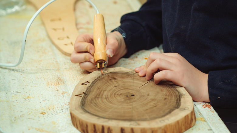 Child'a hand engraving numbers on wood slice clock