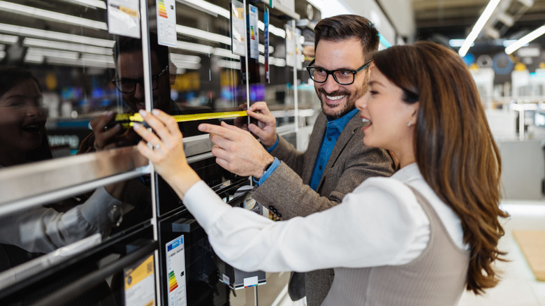 A man and a woman measuring an oven in the store