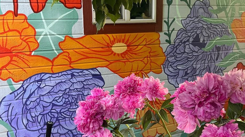 A wall mural painted along the side of the house with colorful flowers on the painting and in front