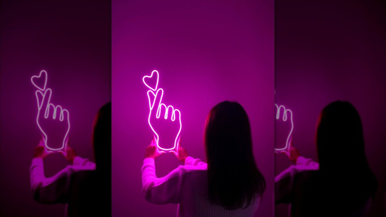 A woman is hanging a neon sign on a wall