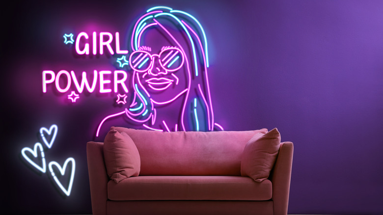 A big neon sign reading Girl Power, with a depiction of a woman, behind a sofa