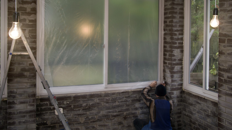 Worker installing insulation film on window.