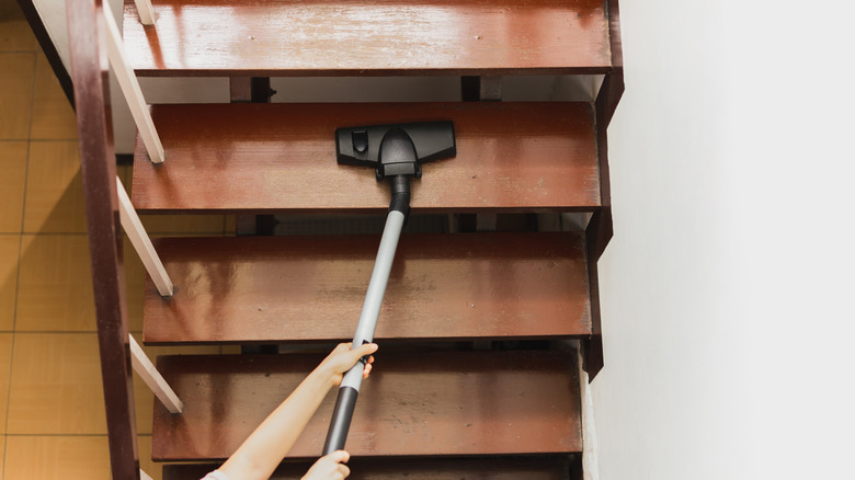 Woman hands vacuuming wooden stairs above a yellow tile floor