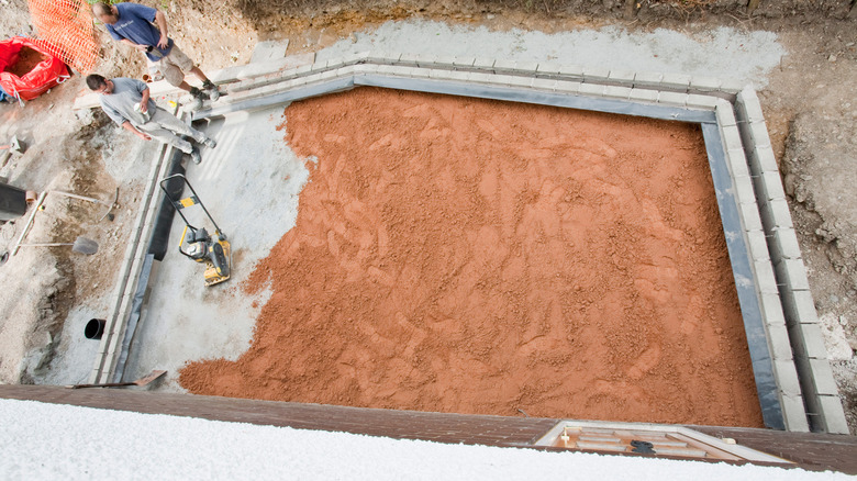 People preparing a sand base before pouring concrete