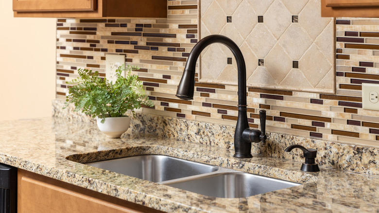 A kitchen sink with an earth-toned glass and stone tile backsplash