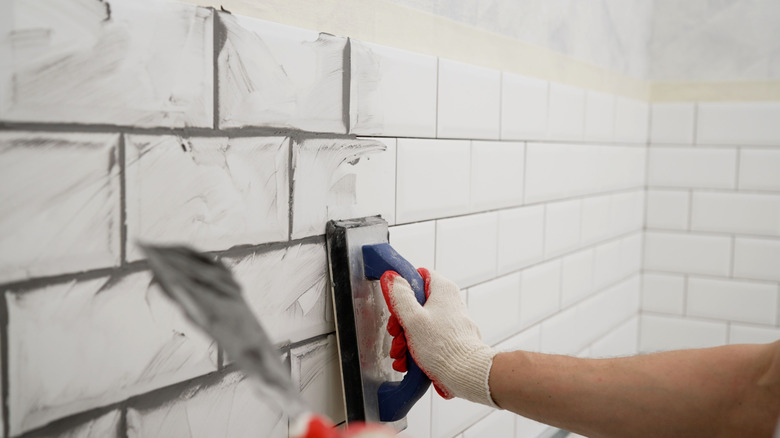 A person applying grout to tiles on the wall