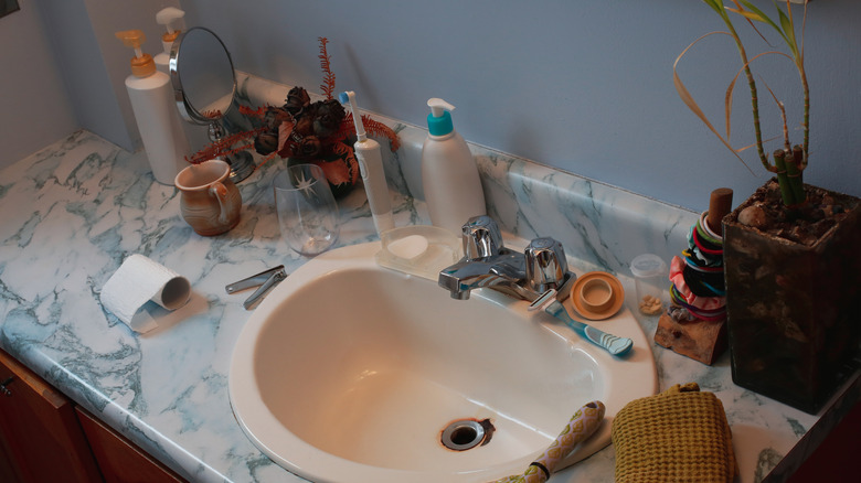 Cluttered bathroom countertop with mirror, hygiene products, and decorative elements