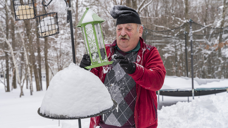 Man clearing bird feeder of snow