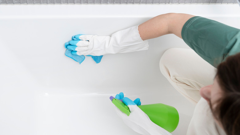 Woman cleaning bathtub with cloth and spray bottle