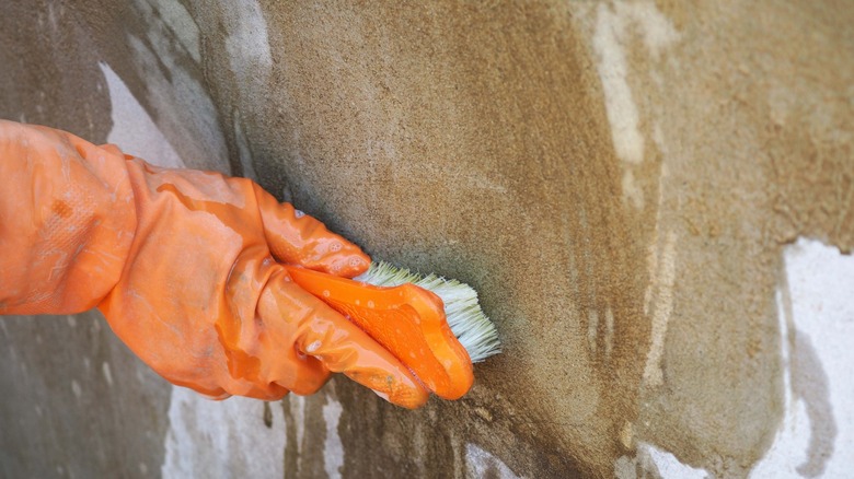 Gloved hand scrubbing concrete surface with brush