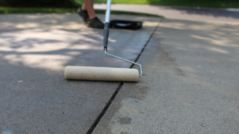 A person applying sealant to a concrete driveway