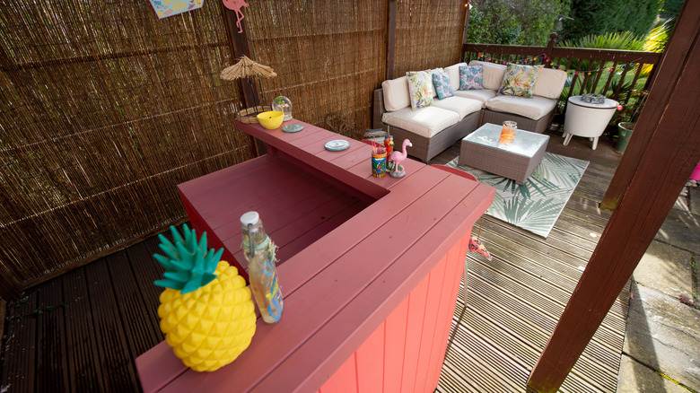 Pinkish outdoor bar with plush furniture, bamboo wall, and plants