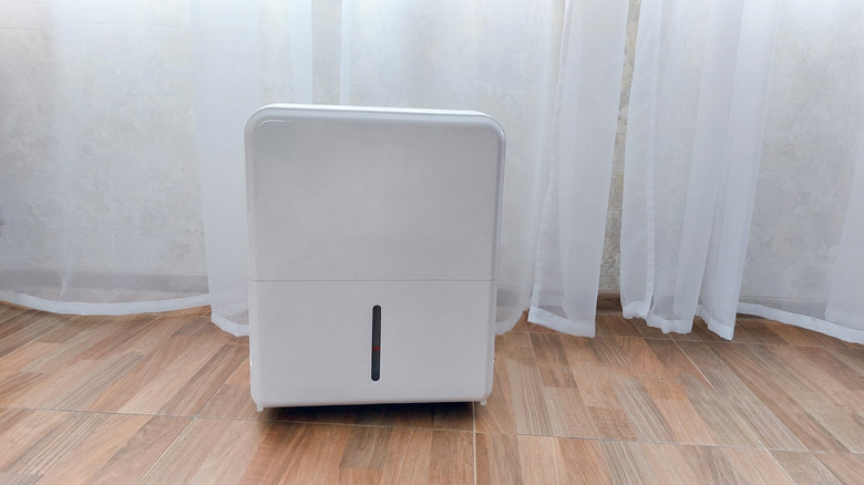 A dehumidifier in front of curtains in a room.