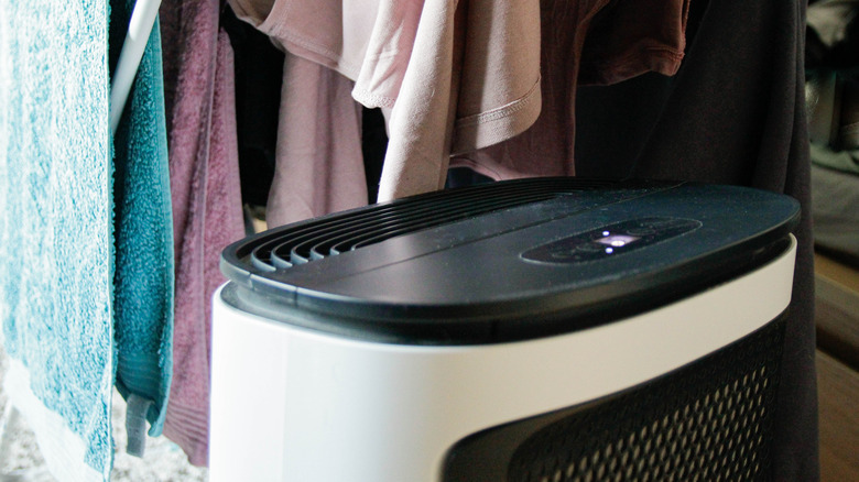 A dehumidifier in a closet underneath clothing.