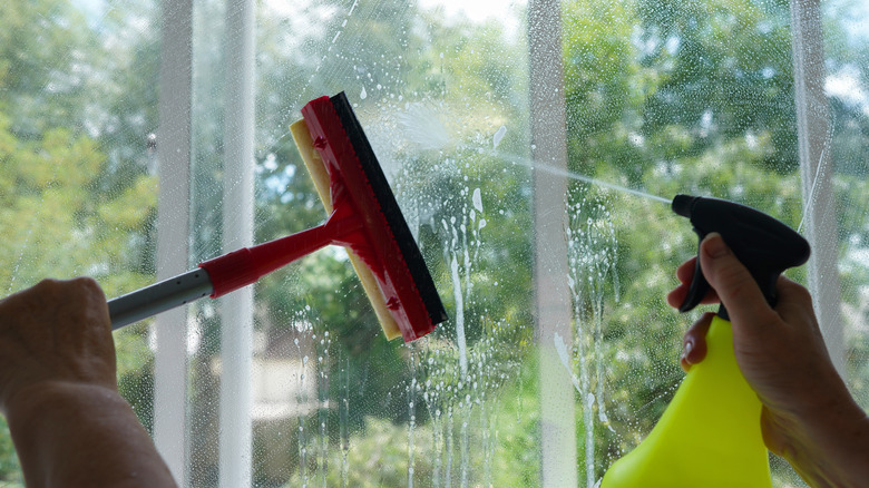 A person is cleaning the inside of a window using a squeegee and a spray bottle