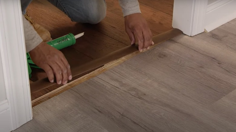 A person installing a wooden transition in a doorway