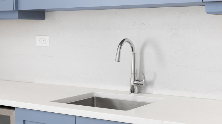 A kitchen sink with an outlet in the middle of a slab backsplash