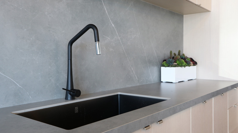 A black sink and faucet against a gray countersplash