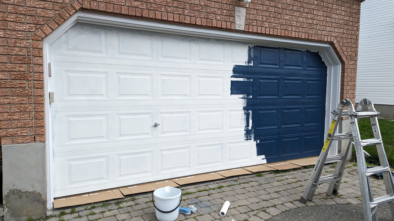 Partially painted garage door with blue paint on brick house