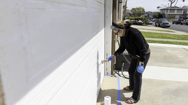 Person painting garage door white with paintbrush