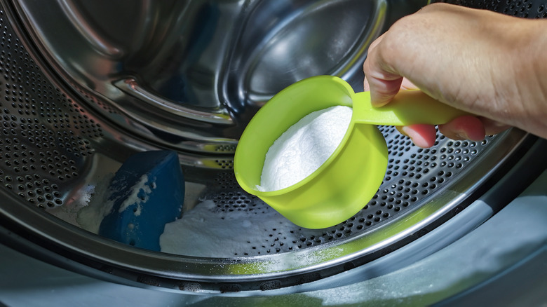 Hand scooping baking soda into washer