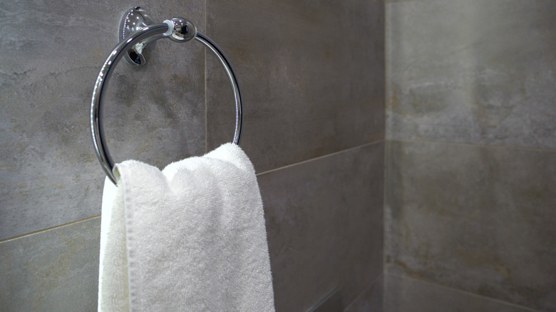 A fresh white towel hangs on a sleek metal towel ring on an elegant gray tiled bathroom wall