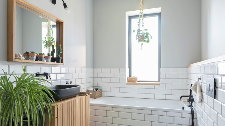 A modern bathroom with white tiles, greenery, and natural light