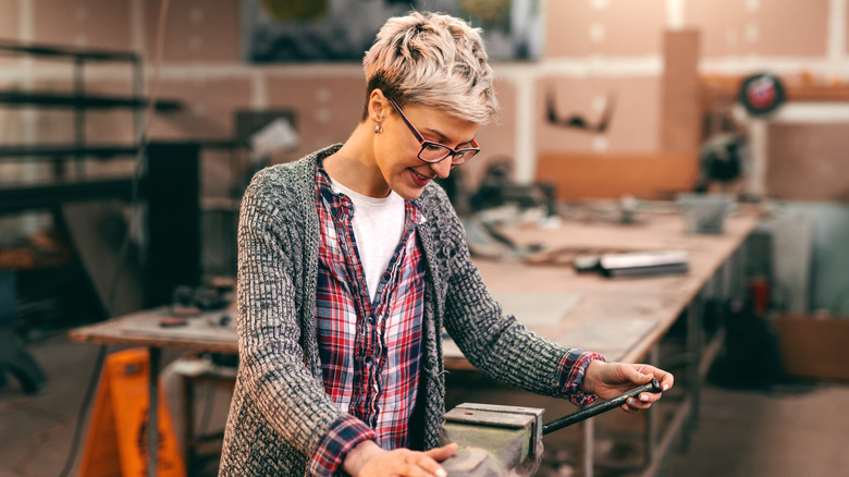 A smiling woman wearing an working with clamp in workshop