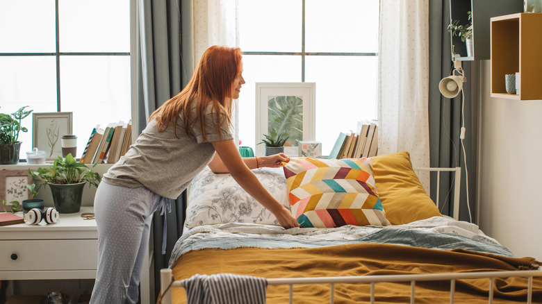 Someone adding a decorative pillow to her bed