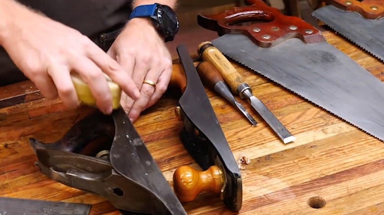 man rubbing wax paste on hand planer on table with other woodworking tools