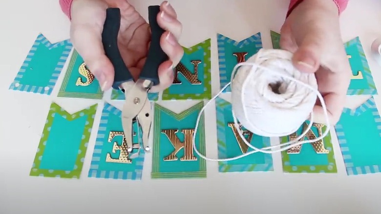 Person crafting business cards into a banner holding a hole punch and ball of twine