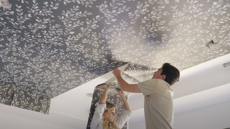 Couple installing wallpaper on ceiling