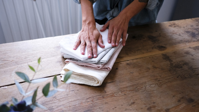 A person is folding cloth napkins on a wooden table.