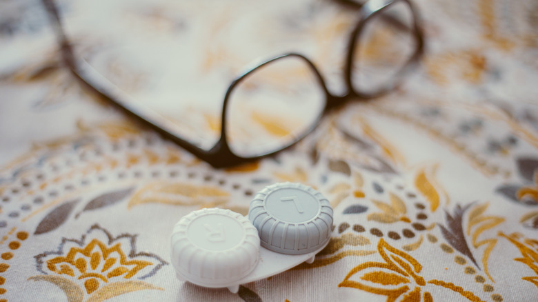 A pair of eyeglasses and a contact lens case on an embroidered fabric