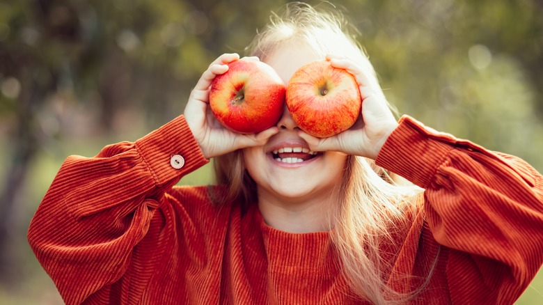 Child holding apples to her eyes 