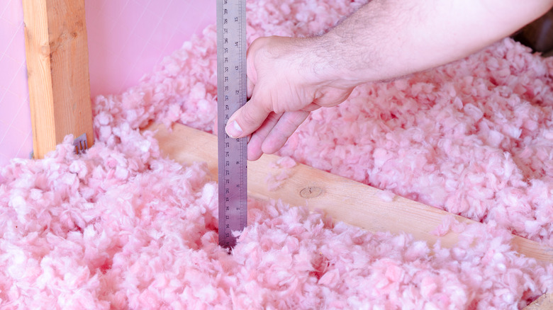 Person measuring the depth of blown-in fiberglass for insulating attic floor