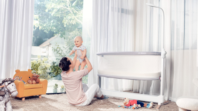 Parent seated on floor holding up smiling baby next to the Revol smart crib