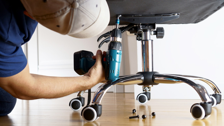 Man unscrewing screws on an office chair base with drill