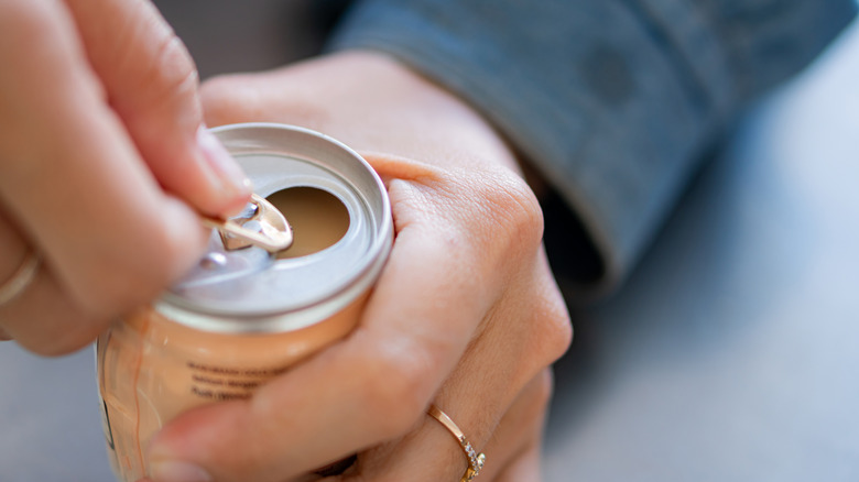 A person opens a soda can by pulling the tab