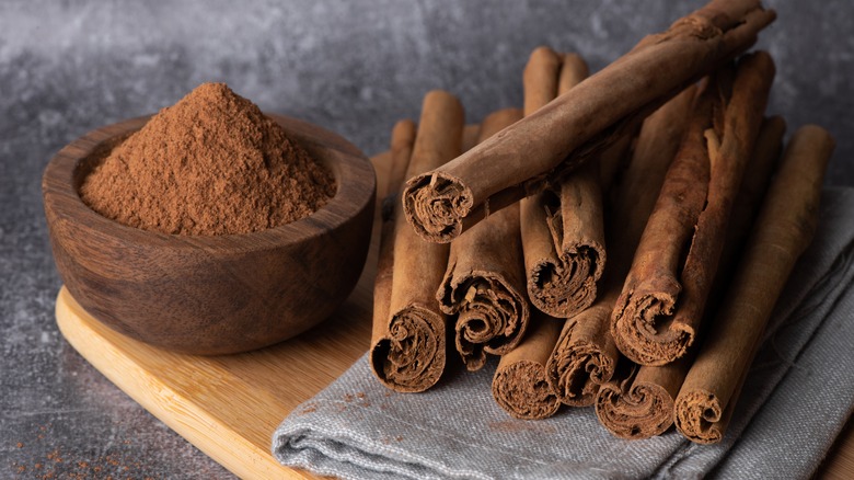 A bowl of cinnamon next to stack of cinnamon sticks