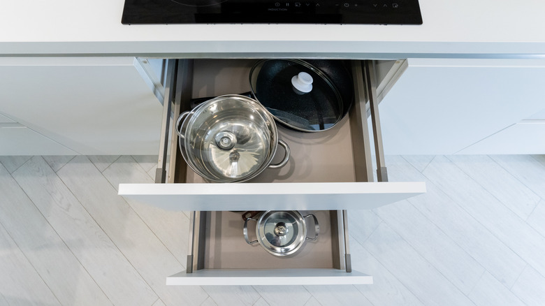 Drawers containing pots, lids, and a steel colander in a white kitchen