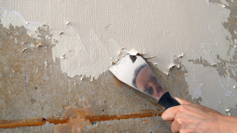 person scraping off wallpaper