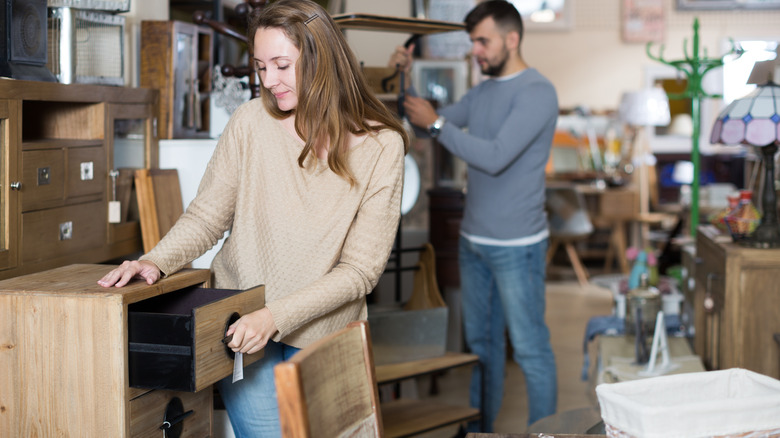 A woman inspects a secondhand wooden cabinet with her partner in the background.