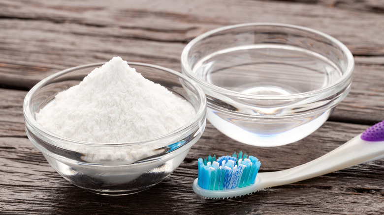 A toothbrush next to two small bowls of baking soda and vinegar