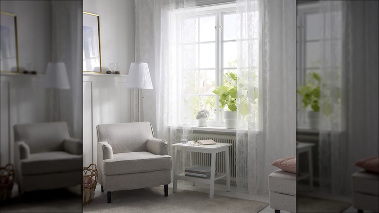 An armchair sits next to a window covered by sheer curtains